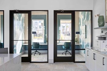A modern office with glass doors leading to a balcony at The Quinn Luxury Apartments, Pensacola, Florida
